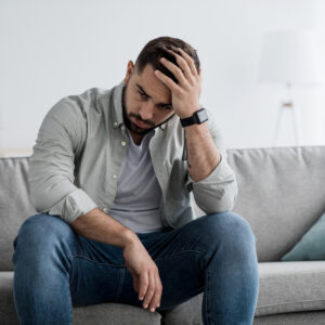 An upset man on a couch in an article on understanding a bulimia diagnosis on the Eating Disorder Recovery Specialists website.